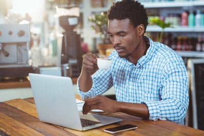Man using a laptop while having cup of coffee in cafe